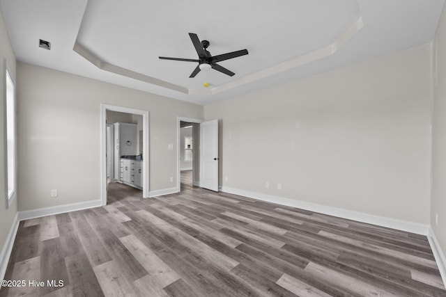 unfurnished bedroom with visible vents, ceiling fan, a tray ceiling, baseboards, and wood finished floors