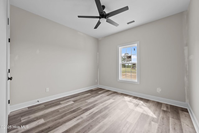 spare room featuring wood finished floors, ceiling fan, visible vents, and baseboards
