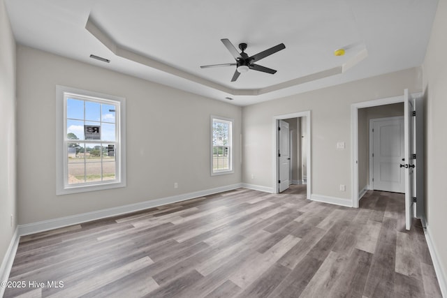 unfurnished bedroom featuring visible vents, baseboards, wood finished floors, and a tray ceiling
