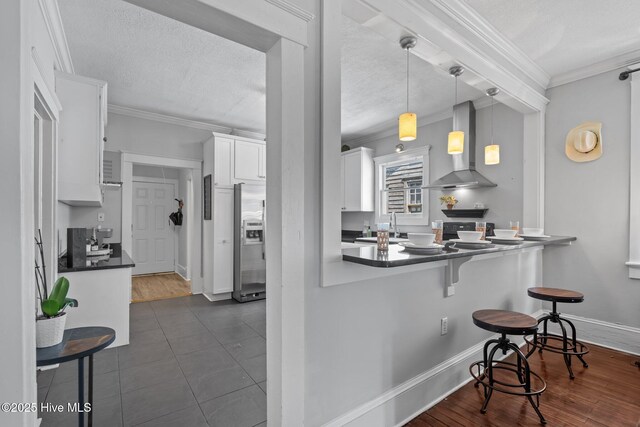 210 S 17th St, Wilmington, NC 28401 - kitchen with wall chimney range hood, stainless steel fridge, white cabinets, a kitchen breakfast bar, and crown molding