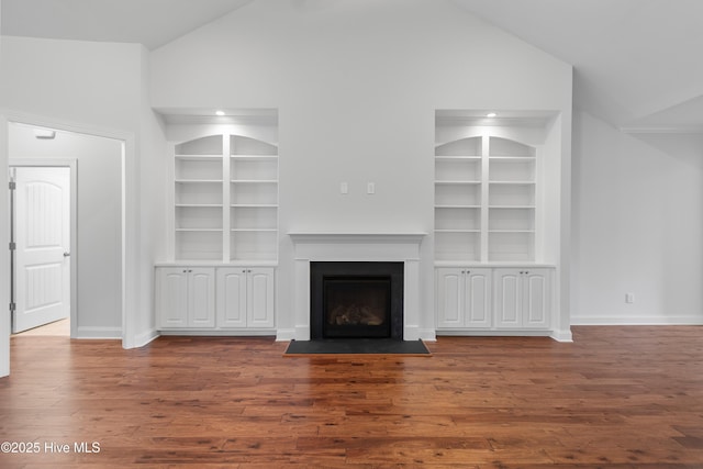 unfurnished living room featuring baseboards, high vaulted ceiling, wood finished floors, and built in shelves