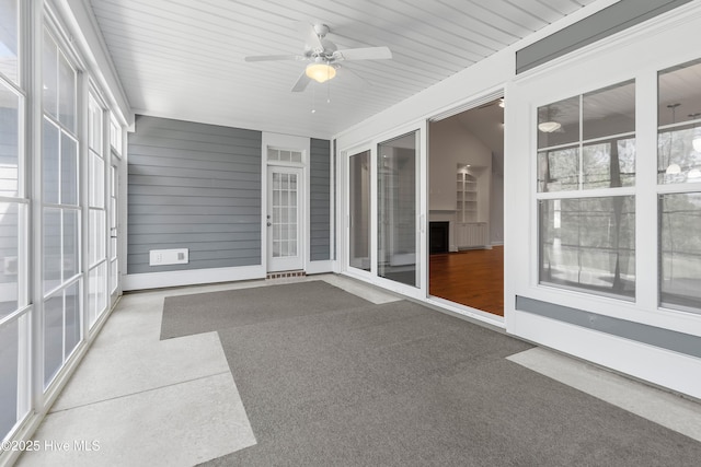unfurnished sunroom with a healthy amount of sunlight, ceiling fan, and a fireplace