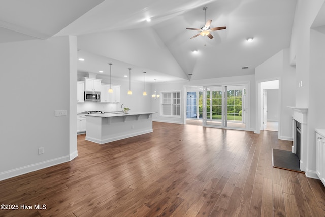 unfurnished living room featuring visible vents, high vaulted ceiling, a fireplace with raised hearth, a ceiling fan, and dark wood finished floors
