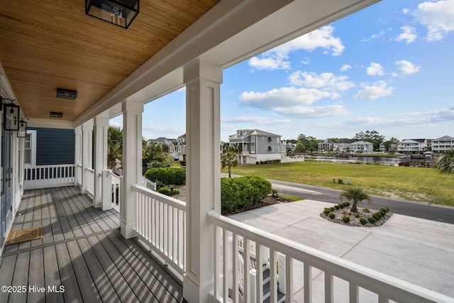 deck featuring covered porch, a residential view, a water view, and a lawn