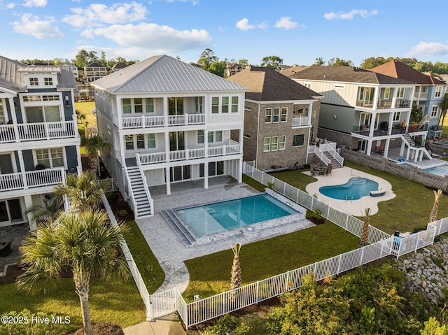 back of house with a fenced backyard, metal roof, a fenced in pool, a residential view, and stairs