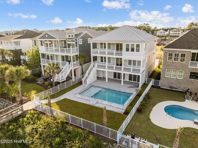rear view of property featuring a fenced backyard, metal roof, a fenced in pool, a balcony, and stairs