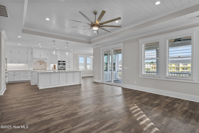 unfurnished living room featuring ceiling fan, a tray ceiling, baseboards, dark wood-style flooring, and ornamental molding