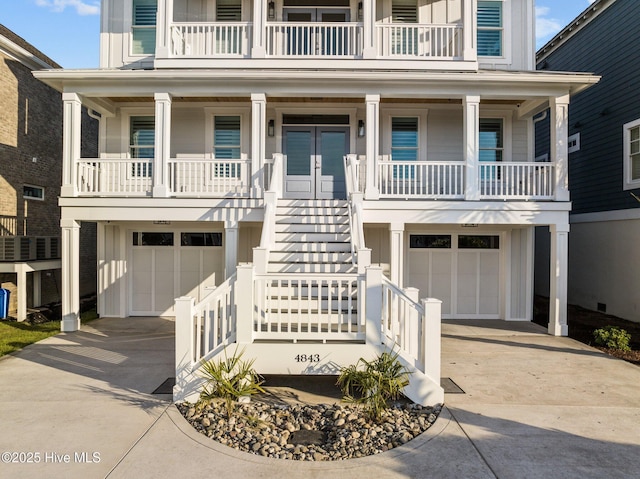 raised beach house with a porch, stairs, concrete driveway, and an attached garage