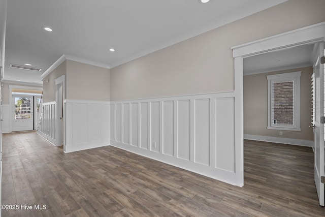 empty room featuring crown molding, wainscoting, a decorative wall, and dark wood-type flooring