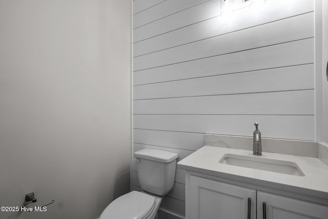 half bath featuring wooden walls, toilet, and vanity