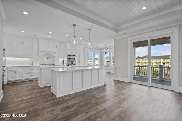 kitchen with an island with sink, dark wood-style flooring, baseboards, a notable chandelier, and crown molding