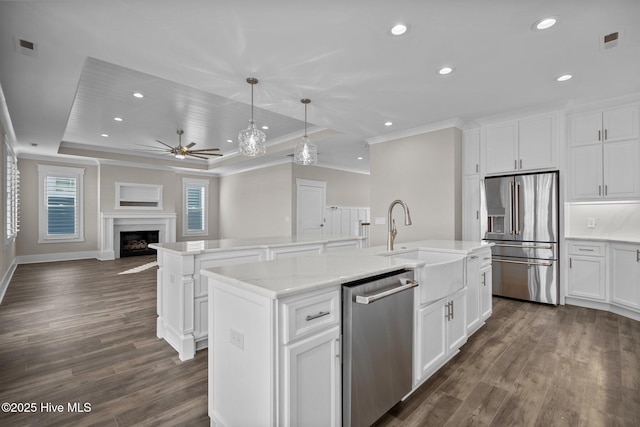 kitchen featuring a center island with sink, appliances with stainless steel finishes, a sink, crown molding, and a tray ceiling