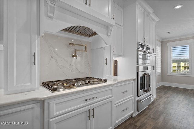 kitchen with dark wood finished floors, stainless steel appliances, a warming drawer, white cabinets, and premium range hood