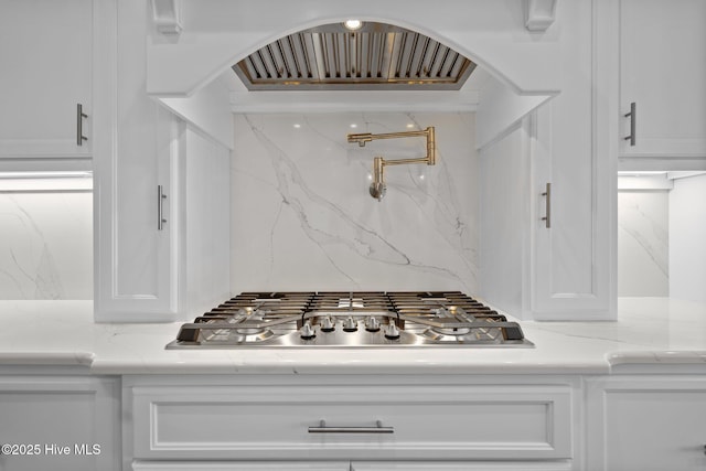 interior details featuring stainless steel gas stovetop, light stone countertops, white cabinets, and arched walkways