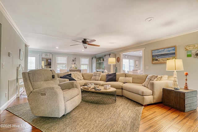 living room with a wealth of natural light, visible vents, crown molding, and light wood-style flooring
