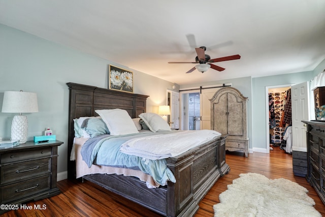 bedroom with dark wood-style floors, ceiling fan, baseboards, and a spacious closet