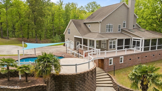 back of property with a chimney, a patio, an outdoor pool, a sunroom, and roof with shingles