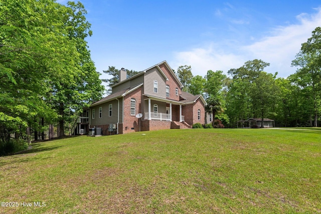 view of front of home with a chimney, brick siding, central AC, a front yard, and a porch