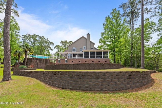 back of house with a sunroom, a chimney, and a lawn