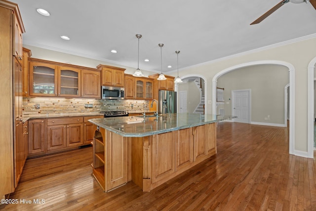 kitchen with a ceiling fan, brown cabinetry, arched walkways, appliances with stainless steel finishes, and ornamental molding