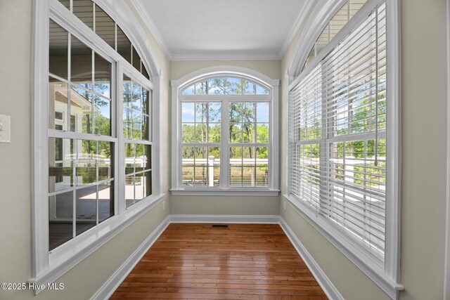 unfurnished sunroom featuring wood-type flooring, visible vents, baseboards, and ornamental molding