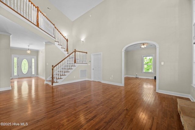 unfurnished living room featuring stairway, visible vents, a towering ceiling, and hardwood / wood-style flooring