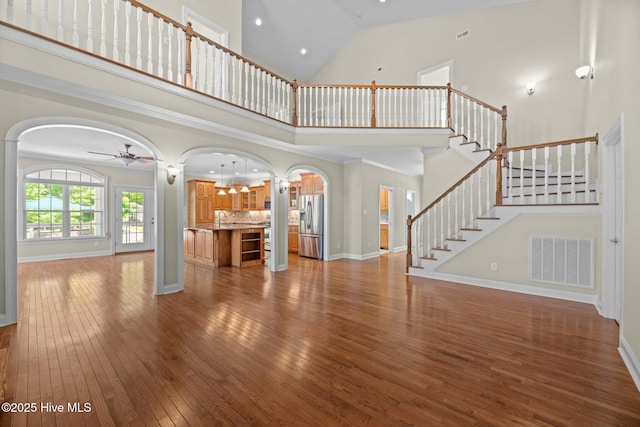 unfurnished living room featuring a high ceiling, wood-type flooring, visible vents, ceiling fan, and arched walkways