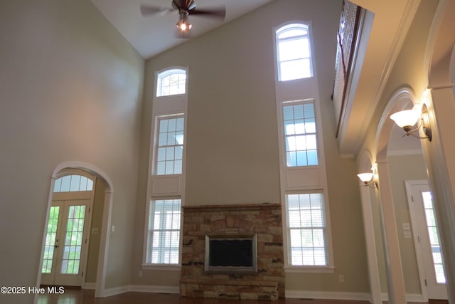 unfurnished living room featuring arched walkways, ceiling fan, baseboards, and high vaulted ceiling