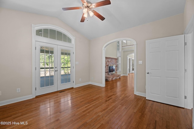 interior space with lofted ceiling, a ceiling fan, french doors, wood-type flooring, and arched walkways