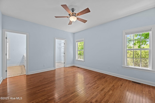 unfurnished bedroom with connected bathroom, baseboards, hardwood / wood-style floors, and visible vents