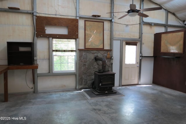 unfurnished living room featuring ceiling fan, a wood stove, a healthy amount of sunlight, and concrete floors
