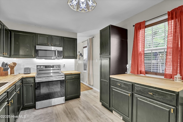 kitchen featuring light wood finished floors, stainless steel appliances, decorative backsplash, a notable chandelier, and wooden counters