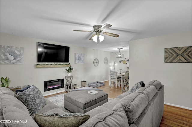 living room with a glass covered fireplace, wood finished floors, a ceiling fan, and baseboards