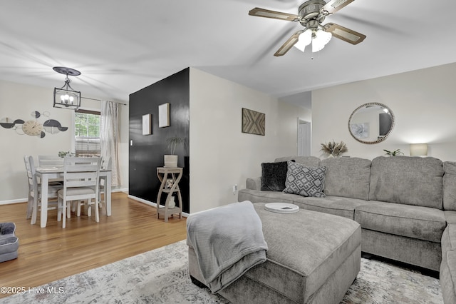 living room with baseboards, ceiling fan with notable chandelier, and light wood-style floors