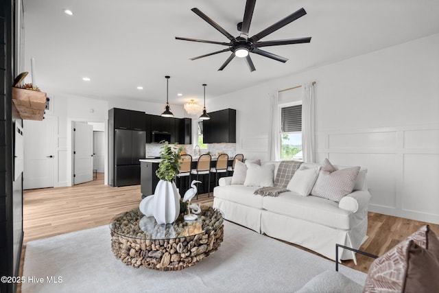 living room featuring a ceiling fan, recessed lighting, light wood finished floors, wainscoting, and a decorative wall