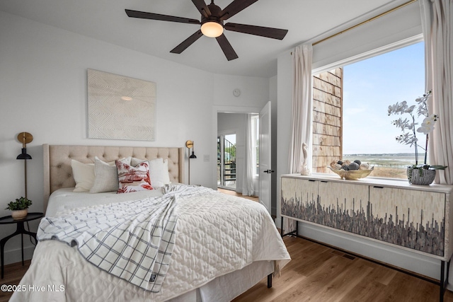 bedroom featuring a water view, a ceiling fan, and wood finished floors