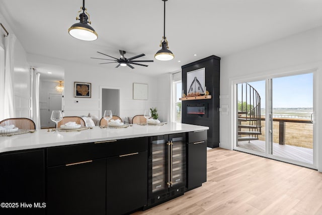 kitchen with light countertops, beverage cooler, dark cabinetry, hanging light fixtures, and light wood-style floors