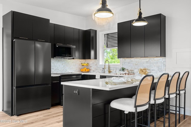 kitchen featuring a peninsula, dark cabinets, freestanding refrigerator, light countertops, and black microwave