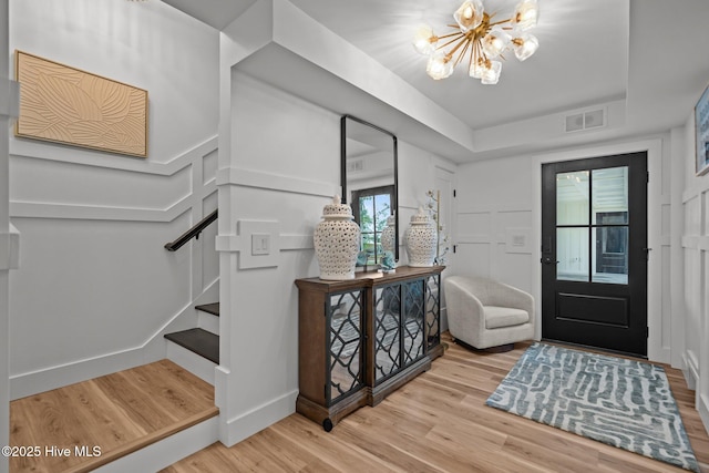 foyer entrance with stairs, wood finished floors, visible vents, a chandelier, and a raised ceiling