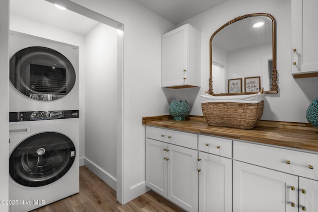 laundry area featuring cabinet space, stacked washer and clothes dryer, baseboards, and light wood-style floors