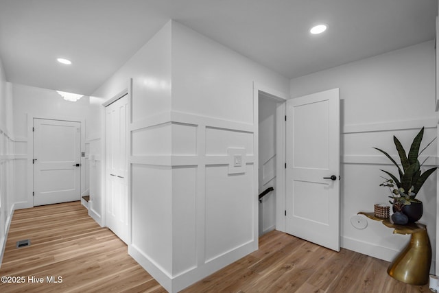 corridor with light wood-type flooring, visible vents, a decorative wall, and recessed lighting