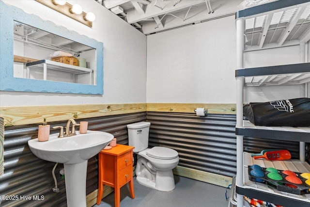 bathroom featuring a sink, finished concrete flooring, wainscoting, and toilet