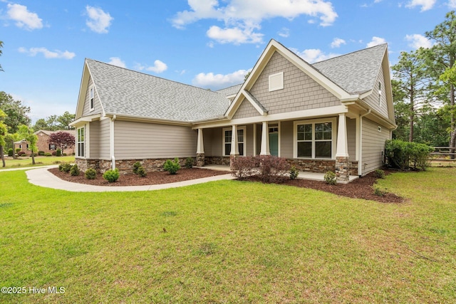craftsman house featuring roof with shingles, a front yard, and stone siding