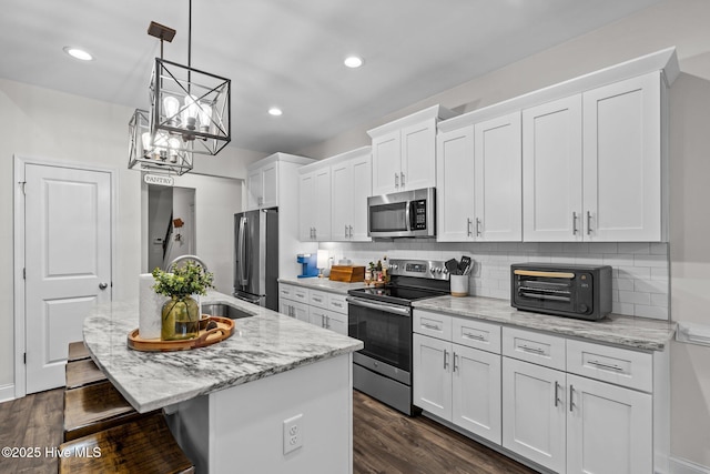 kitchen with a kitchen island with sink, appliances with stainless steel finishes, a sink, white cabinets, and a breakfast bar