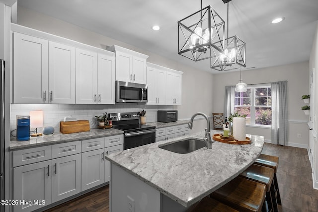 kitchen with a kitchen island with sink, dark wood-style flooring, tasteful backsplash, a sink, and stainless steel appliances