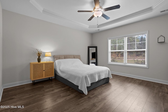 bedroom featuring dark wood finished floors, baseboards, a tray ceiling, visible vents, and ornamental molding