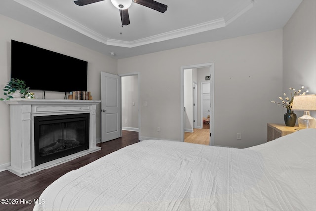 bedroom featuring a ceiling fan, crown molding, wood finished floors, baseboards, and a glass covered fireplace