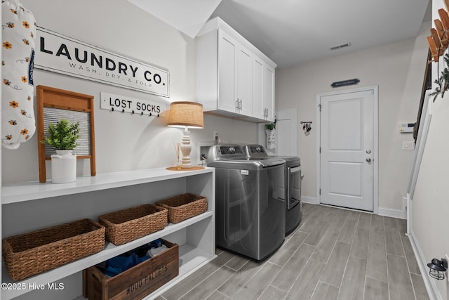 laundry area featuring wood tiled floor, visible vents, cabinet space, baseboards, and separate washer and dryer