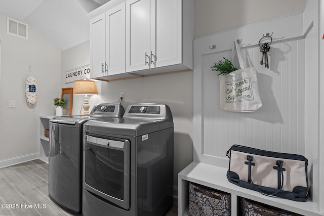 washroom with visible vents, cabinet space, baseboards, light wood-style floors, and washer and clothes dryer