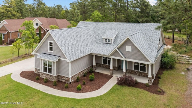 craftsman-style home featuring a shingled roof, a front lawn, covered porch, and stone siding